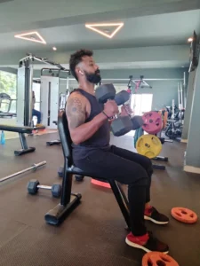 Person performing seated dumbbell shoulder press exercise at Torque Fitness Mysore