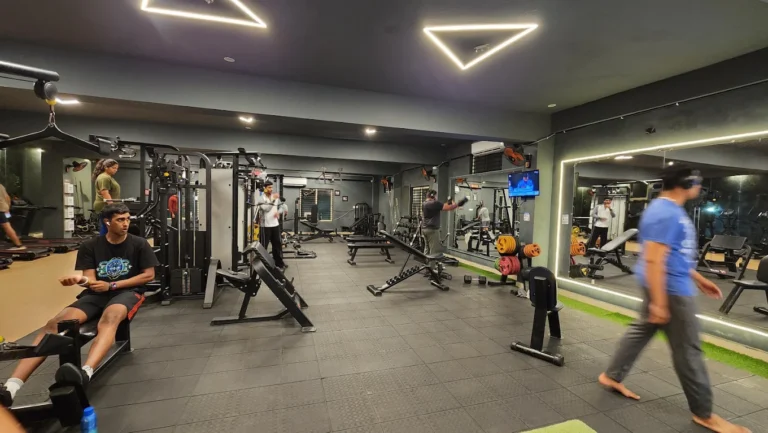 Beginners performing weight training exercises including lateral raises, lat pulldown and triceps pushdown at a gym in Mysore