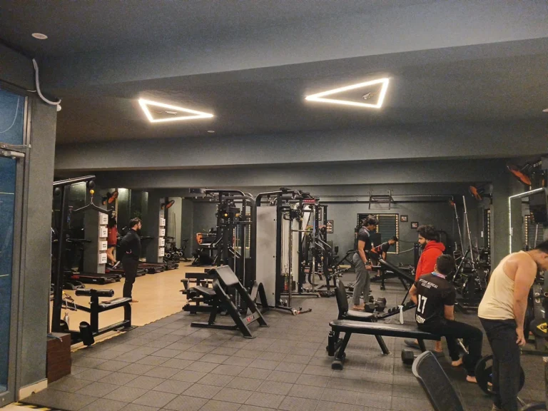 Male beginners doing weight lifting exercises in front of mirrors at a gym in Mysore